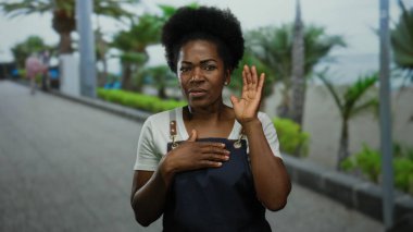 Önlük giymiş bir kadın sahilde palmiye ağaçlarıyla dikiliyor. Sahilde yürürken ve konuşurken, sakin bir okyanus manzarasıyla duyguları iletiyor..