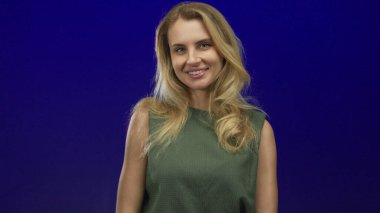 Genç sarışın kadın canlı mavi arka plana gülümsüyor. Kendine güven ve pozitiflik gösteriyor..