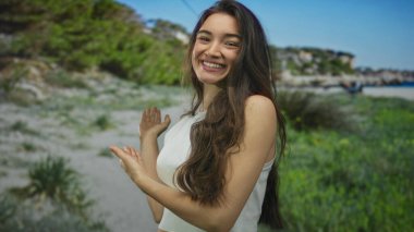 Uzun saçlı genç İspanyol kadın güneşli sahildeki güneşli kumlu sahilde avuçlarını açık gösteriyor..