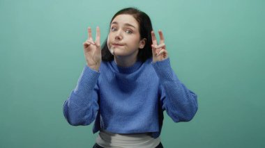 Mavi süveter giymiş, yeşil arka planda hareket eden ve elleri rahat bir şekilde vurgu yapan bir kadın..