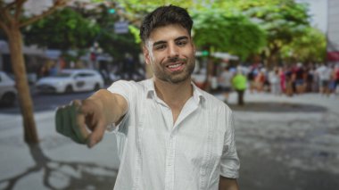 Beyaz keten gömlekli İspanyol adam gülümsüyor ve güneş ışığı sokağındaki kamerayı işaret ediyor..