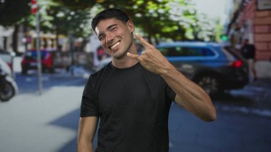 Siyah tişörtlü İspanyol genç adam hareketli şehir caddesinde taş boynuzları, rock eğlenceli metal.