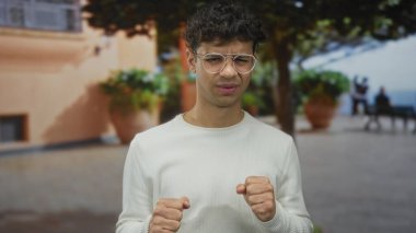 Gözlüklü adam ve beyaz süveter giyen adam kalabalık şehir caddesinde gözler ve yumruklar sıkar; rahatsızlık.