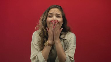 Şaşırdığını ve heyecanlı olduğunu ifade eden bir kadın geniş gözlü, açık ağızlı ve canlı kırmızı arka planda nötr bir kıyafet giymiş..