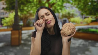 Parktaki kadın beyin modelini tutuyor ve yeşil yapraklı ağaçların altında el ele ağlıyor. Üzüntü ve düşünce duygularını paylaşıyor..