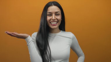 Beyaz bluzlu, neşeli, uzun saçlı, parlak turuncu arka planda gülümseyen İspanyol kadın, neşeli hareketleriyle şaşkınlığını dile getiriyor..