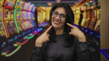 Orta yaşlı İspanyol kadın kumarhanedeki parlak kumar makinesinin yanında yanakları işaret ediyor..