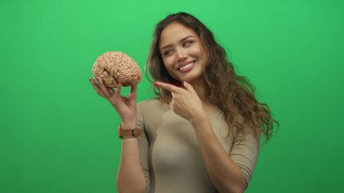 Beyin modelini yeşil arka planda tutan kadın kendine güvenen bir ifadeyle zeka odaklanma ve bilgi gösteriyor.