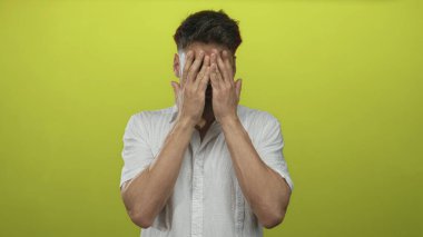 Beyaz gömlekli genç adam sarı bir stüdyoda ellerini öne uzatıyor ve göğsünü sıkıca tutuyor; acıdan kaçınıyor..