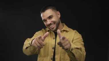 Sarı tişörtlü, geniş ve enerjik bir şekilde gülümseyen İspanyol genç stüdyoyu işaret ediyor..