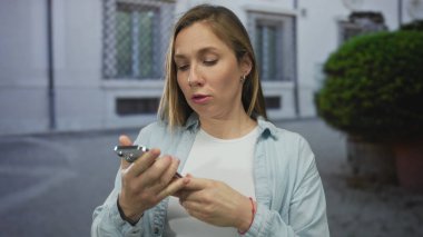 Dışarıdaki kadın, şehir ortamında elinde telefonla, gün ışığında duygu ve tepki gösteren bitkilerle hayal kırıklığını ifade ediyor..