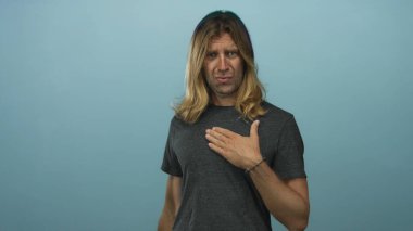 Stüdyoda eli göğsünde olan sarışın bir adam odaklanmış bakışlarını ve ince duruşunu gösteriyor..