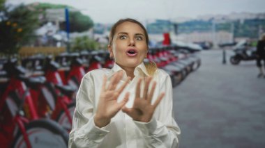 Dışarıdaki bisiklet parkındaki beyaz tişörtlü, arka planda bulanık bisikletler ve ağaçlarla hareketli bir an yakalayan bir kadın..