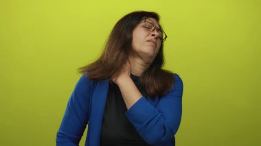 Stüdyoda boyunluk takan, limon yeşili arka planlı bir kadın boyun gerilmesine işaret ediyor..