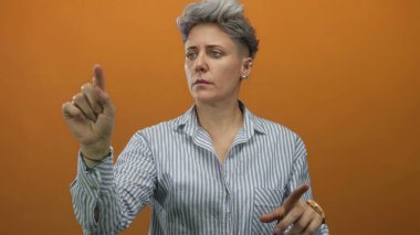 İşaret parmağını diğer eliyle turuncu stüdyo arka planına doğru uzatan kadın, konsantrasyon belirleme odağı.