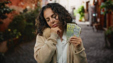 Bir şehir caddesinde elinde Romanya banknotları tutan orta yaşlı bir kadın dinginlik ve tefekkür ifadesiyle bir anlık finansal yansımayı yakalıyor..