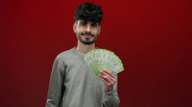 Elinde Rus rublesi banknotları tutan adam canlı kırmızı bir arka plana gülümsüyor zenginlik ve para gösteriyor..