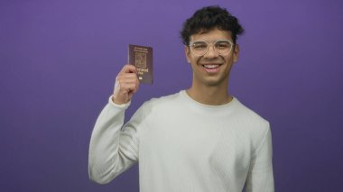 Gözlüklü bir adam stüdyoda gülümsüyor ve elinde mor duvarlı bir pasaport tutuyor; küresel kimlik hareketliliği umudu.