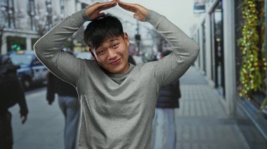 Genç adam şehrin bir caddesinde mutlu bir şekilde dikiliyor, bir şehir zeminine karşı Çin mirasını sergiliyor, açık havada keyif ve kültür anı yakalıyor..