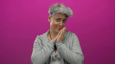 Bir kadın pembe stüdyo ortamında iki eliyle yüzünü diş ağrısı için bastırırken yanaklarını tutuyor; belirsizlik.