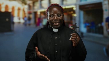 Şehir caddesinde haçı olan kadın rahip şehir ortamında inanç ve maneviyat aktarıyor, çeşitliliği ve dini bağlılığı vurguluyor..