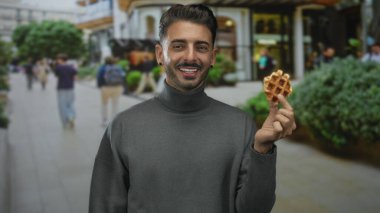 Waffle tutan adam gülen yüz ile şehir caddesinde el hareketi göstererek waffle; aşçılık neşe.