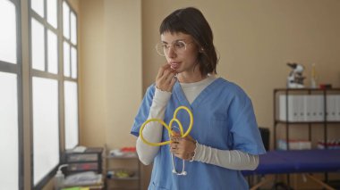Gözlüklü kadın hemşire klinik binasında sarı steteskop ayarladı; sakin şefkat gösterme bakımı.