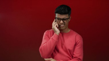 Kırmızı arka planda telefonu olan gözlüklü bir adam merak ve merak ifadesi sergiliyor..