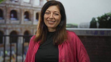 Roma kolezyum binasının önünde gülümseyen pembe ceketli orta yaşlı İspanyol kadın..