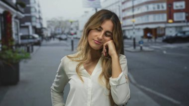 Sarışın genç bir kadın çıplak kollarını açarken gözleri kapalı ve hafifçe gülümserken şehir sokaklarında rahatlama.