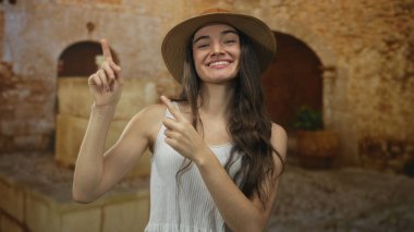 Hasır şapka ve beyaz atlet giyen genç bir kadın eski kentteki güneşli sokağa parmak basıyor..