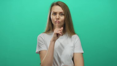 Yeşil arka planda sessizce susan bir kadın, düşünceli bir ifadeyle günlük beyaz bir gömlek içinde sessizliğini koruyor.