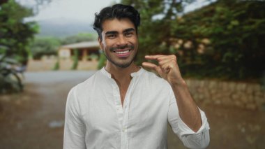 Beyaz gömlekli adam, taş bina görünür eski bir kasaba caddesinde başparmak ve işaret parmağı arasında küçük bir boşluk çimdikler; merak ölçüm detay hassasiyeti.