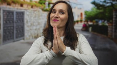 Açık havada ağaçlar ve taş duvarlarla gülümseyen bir kadın güneşli bir günde gökyüzünün altında dostça bir ifade sergiliyor..