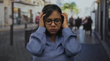 Gözlüklü Afrikalı Amerikalı bir kadın iki eliyle yüzünü buruşturuyor, baş ağrısı çekiyor..