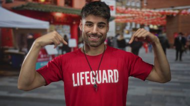 İspanyol adam kırmızı cankurtaran gömleğini işaret ediyor ve kalabalık şehir caddesinde ıslık çalıyor..