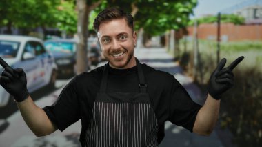 Sakallı ve önlüklü genç bir adam eldivenli elleriyle şehir sokaklarında, bir garson gibi güvenle gülümsüyor..