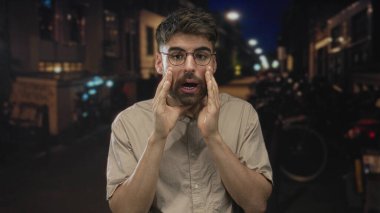 Gece loş aydınlatılmış şehir caddesinde sakallı bardaklı genç adam elleri ağıza dolanıyor. Acil duyuru..