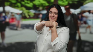 Güneşli bir şehir caddesinde boks yapan kadın, arka planda bulanık yayaların bulunduğu açık şehir ortamında güç ve güç gösterisi yapıyor..