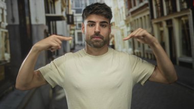 İspanyol asıllı genç adam güneşli bir şehir caddesinde kendini işaret ederek bina cephelerinin etrafını sardı..