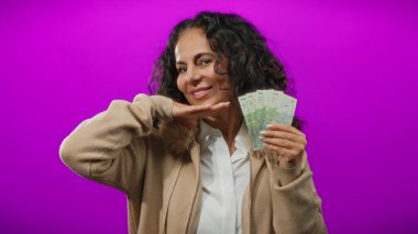 Romen banknotlarını elinde tutan orta yaşlı bir kadın canlı bir mor arka plana karşı, neşeli bir ifadeyle para sergiliyor..