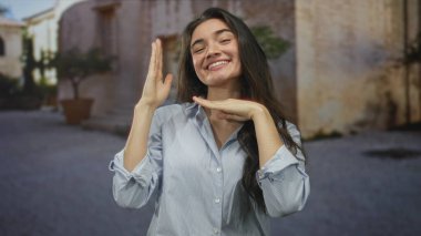 Mavi gömlekli kadın eski sokakta avuç içi çene altı jest ile gülümsüyor; dinginlik güven cazibesi.