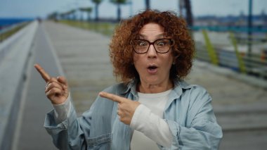 Orta yaşlı, esmer, kıvırcık saçlı ve gözlüklü bir İspanyol kadın deniz kenarında gezinirken heyecanla el kol geziyor, açık deniz ortamında sürpriz ve neşe saçıyor..