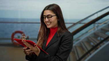 Gezgin gemisinde elinde gözlük ve açık havada kırmızı süveter ile gülümseyen bir kadın liman kenarında deniz yolculuğu yapıyor ve uzun saçlı modern moda.