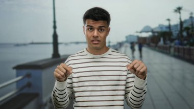 Genç adam deniz kenarındaki bir gezinti alanında sakin bir plaj geçmişine yansıyan rahat ve mizahi bir tavır sergiliyor..