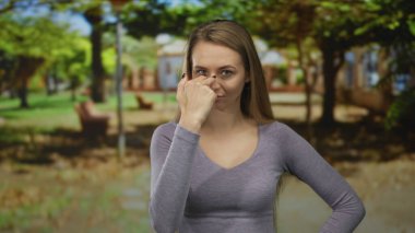 Yeşil bir park ortamında hareketli bir kadın, dikkatli ifadeler ve ağaçların gölgesinde doğal hava koşullarına odaklanmış..