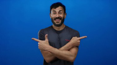 Günlük gömlekli İspanyol bir adam gülümsüyor ve parlak mavi bir arkaplanı işaret ediyor. Olumlu duygular ve gelişigüzel davranışlar sergiliyor..