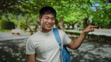 Serin yeşil bir parkta sırt çantasıyla gezen ve gülümseyen genç adam, neşeli ve neşeli bir eğlence ve keşif atmosferi sergiliyor..