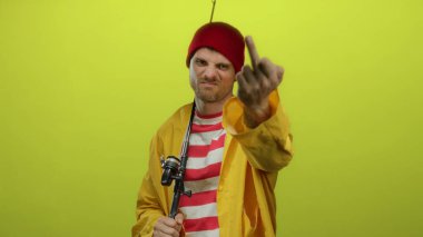 Sarı yağmurluklu İspanyol adam, kırmızı şapkalı. Elinde olta tutarken kaba bir jest yapıyor. Hayal kırıklığı ya da mizah anlayışı gösteriyor.