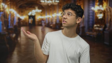 Adam avuç içi kaldırarak elini tutar ve süslü galeri binasındaki mermer heykele bakar; merak.